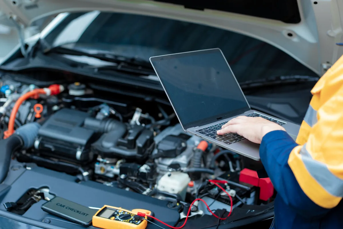 Auto electrician using a laptop to run diagnostics on a car engine bay